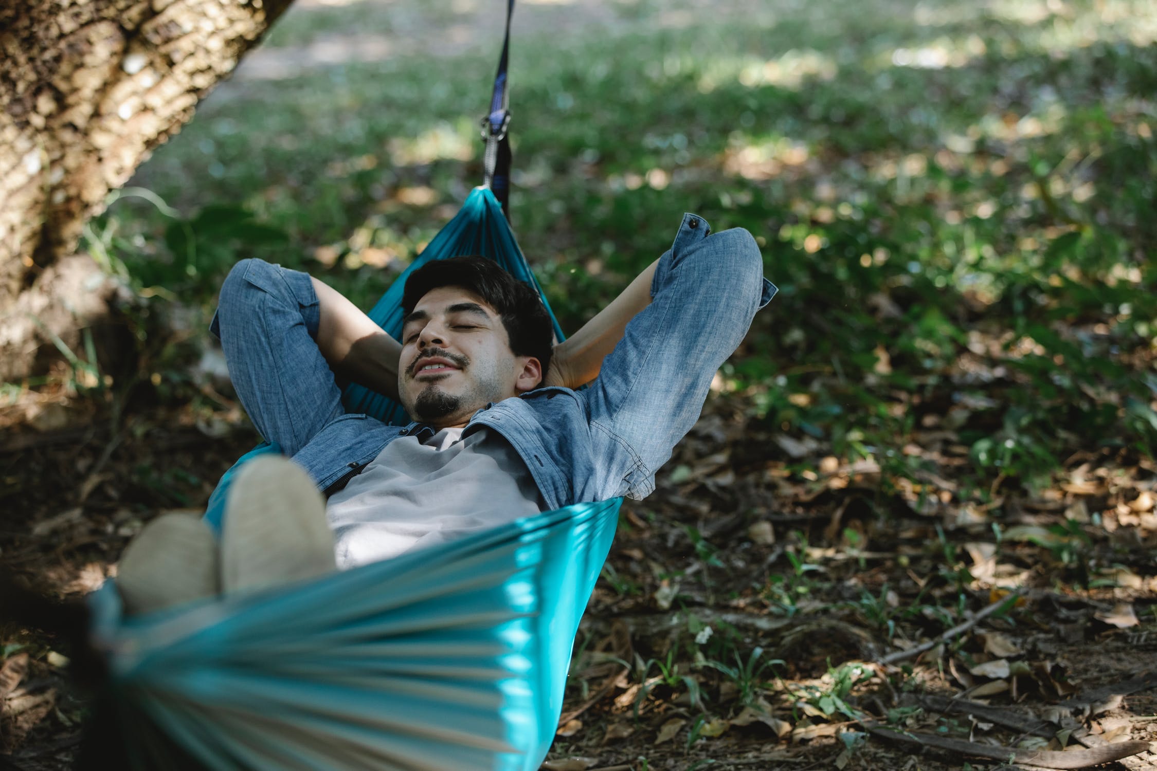 Man lying in a green hammock outside under a tree.